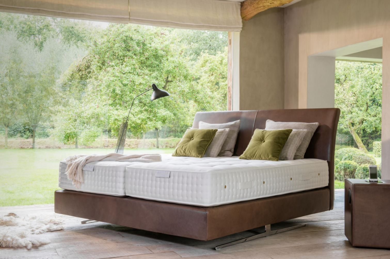 Boxspringbett vor großer Fensterfront mit Blick ins Grüne